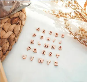 Détail en gros plan de charms alphabet en or rose, pendentif DIY en acier titane brillant.