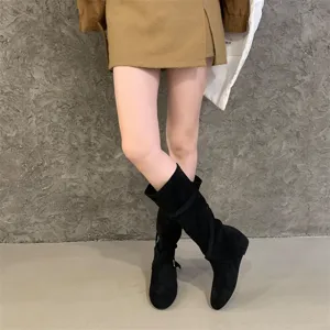 Detailed view of women's suede slouched boots with cross strap buckle and wedge heel design.