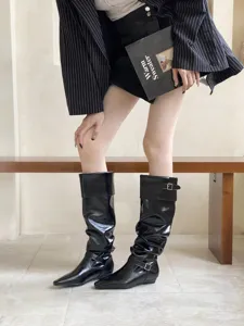 Vista detallada de elegantes botas altas negras arrugadas con tacón bajo y puntera cuadrada.