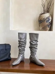Vista detallada de botas altas arrugadas de charol brillante con punta cuadrada y tacón.