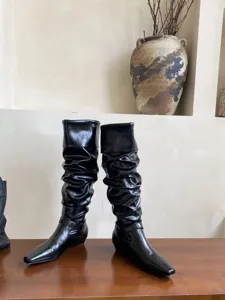 Botas altas negras estilo slouchy con punta cuadrada, tacón bajo y elegante tira en el tobillo.