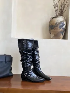 Primer plano de botas altas de cuero negro con diseño fruncido y hebillas metálicas.