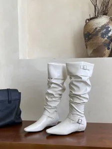 Vista detallada de botas altas arrugadas en color crema con puntera cuadrada y tacón plano.