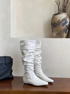 Vista detallada de botas altas arrugadas en blanco crema para mujer con hebilla metalica fina.