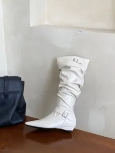 Plano de detalle de botas altas blancas fruncidas con punta fina, hebilla y tacón bajo plano.