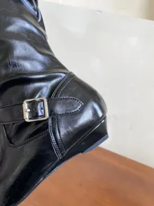 Primer plano de detalles de botas largas negras brillantes de mujer con hebilla y tacón.
