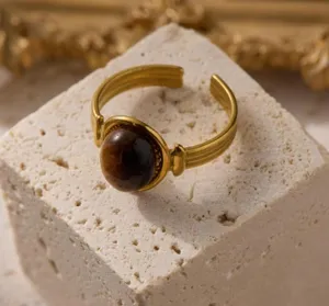 Detailopname van gouden roestvrijstalen ring met bruine edelsteen op getextureerde steen.