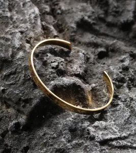 Close-up of minimalist gold-plated stainless steel open cuff bracelet with glossy finish.