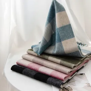Close-up view of folded winter plaid wool scarves on white table, showing soft texture and tassel details.