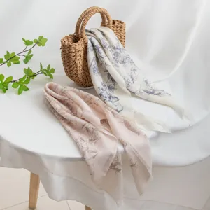 Close-up detail of floral print cashmere scarf styled on straw bag and white tabletop setup.
