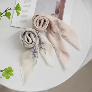 Detailed close-up shot of rolled floral print square scarves on a clean white tabletop surface.
