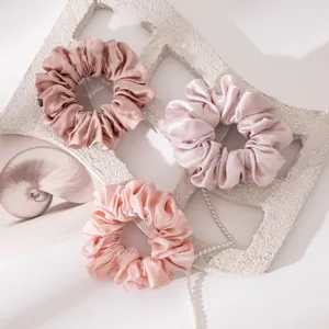 Close-up detail shot of elegant satin silk hair scrunchies in pink with chic pearl chain decor.
