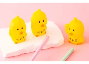 Detail shot of cute yellow duck squeeze toys displayed on a white platform with pink background.