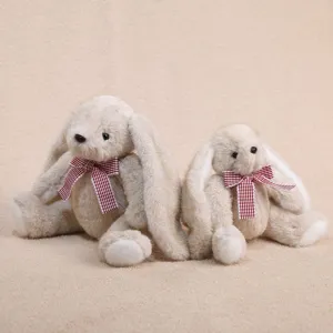 Mignon lapin en peluche assis aux longues oreilles avec nœud papillon à carreaux rouges.