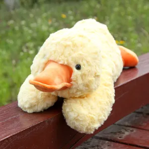 Cute yellow duck plush toy detail view, soft hugging cushion in outdoor green nature scene.