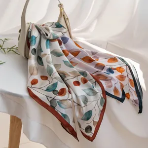 Detailed view of elegant silk square scarf with colorful leaf print draped on handbag.