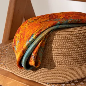 Detail shot of artistic printed silk scarf draped on straw hat, elegant summer neckerchief.