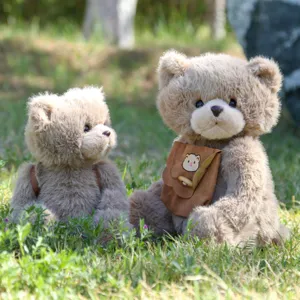 Nahaufnahme eines süßen Plüsch-Teddybären mit kleinem Rucksack auf grünem Gras im Außenbereich.