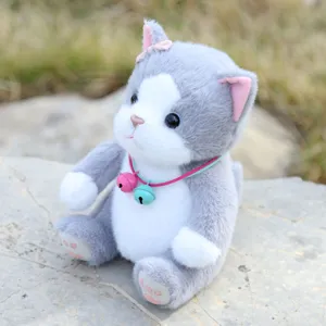 Close-up of cute grey plush cat toy with bells and collar sitting on stone background.