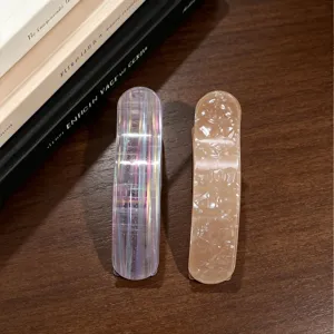 Detail view of curved acetate hair clips featuring iridescent and beige textured barrettes.
