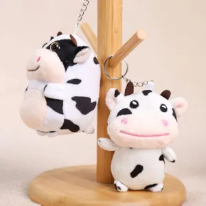 Vista dettagliata portachiavi peluche mucca, morbido ciondolo bianco e nero su supporto legno.