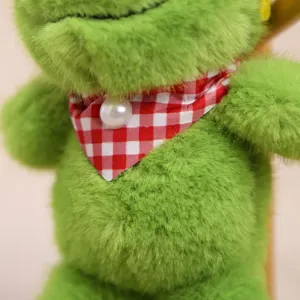 Primer plano detallado de un peluche de rana verde con bufanda de cuadros y perla.