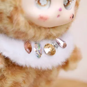 Close-up detail of plush vinyl doll pendant with fluffy white collar and colorful rhinestones.