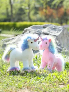 Outdoor detail view of cute rainbow plush unicorn dolls standing on green grass, soft toy.