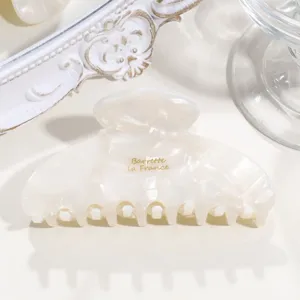 Close-up detail of French acetate hair claw clip, milky crescent design with gold stamp.