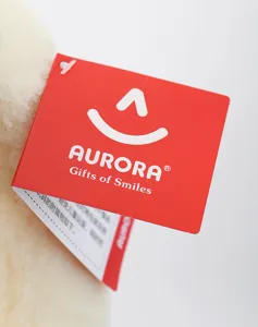 Vista detallada de la etiqueta colgante de la marca de peluche Aurora con logo rojo.
