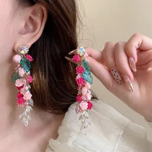 Detailed shot of long floral tassel earrings featuring pink resin roses and sparkling rhinestones.