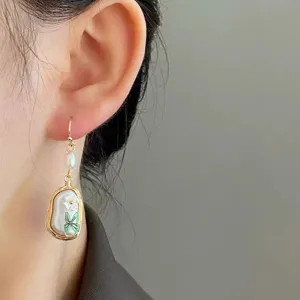 Detail view of gold-tone drop earrings featuring pearl, flower and butterfly charms elegantly.