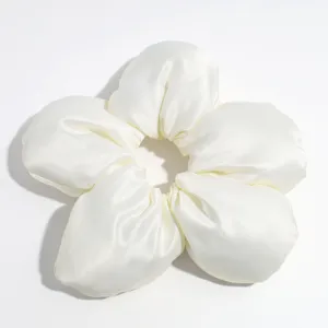 Detaillierte Nahaufnahme des eleganten weißen Satin-Blumen-Haargummis mit weicher Stoffstruktur.