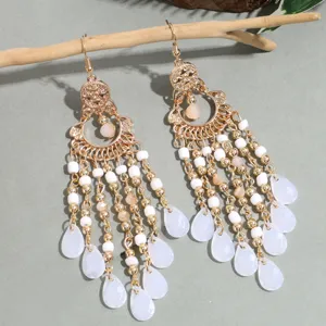 Detailed shot of long gold-tone tassel earrings featuring delicate white beads and teardrop drops.