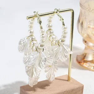 Detailed close-up of elegant faux pearl and white leaf tassel hoop earrings on stand.