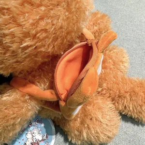 Close up of brown fluffy plush toy detail with zipper pocket, soft texture and cute doll design.