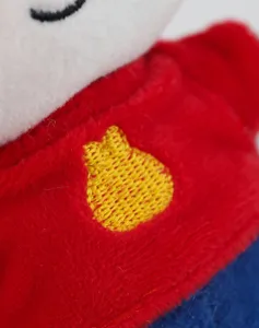 Plush toy detail close-up showcasing soft fabric texture, red sweater and cute yellow embroidery.