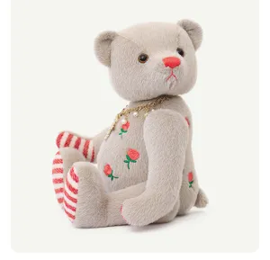 Vista dettagliata dell'orsacchiotto di peluche con ricamo di rose e collana di perle.