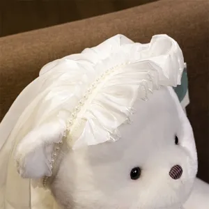 Close-up detail of white plush teddy bear wearing elegant wedding veil and pearl headband.