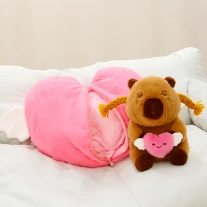 Cute capybara plush toy with braided hair holding pink heart pillow and matching heart wing bag.