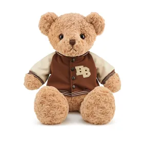 Charmant petit ours en peluche portant une veste universitaire marron et blanche.