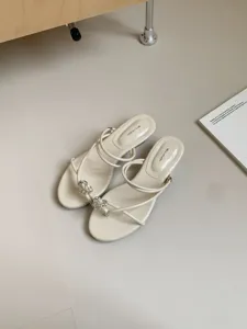 Vue rapprochée détaillée de sandales blanches à talons hauts, fines brides et cœur en cristal.