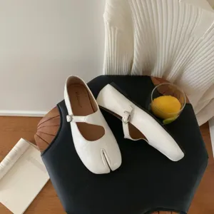 Close-up detail of white split toe Mary Jane flat shoes with strap and soft leather finish.