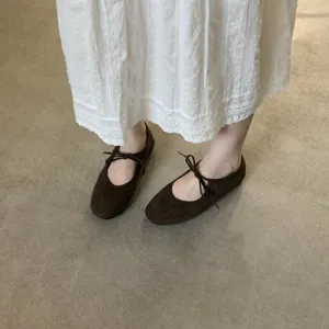 Detail shot of brown suede lace-up ballet flats paired with a white dress on a clean floor.