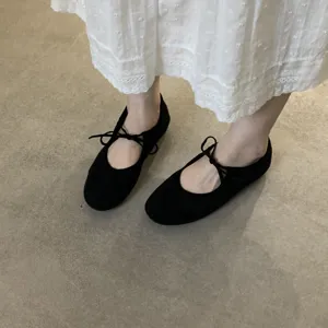 Close-up shot of black soft suede ballet flats with delicate string bow detail on feet.