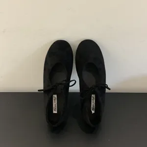 Close-up detail shot of black lace-up bow ballet flats, highlighting soft sole and inner tag.