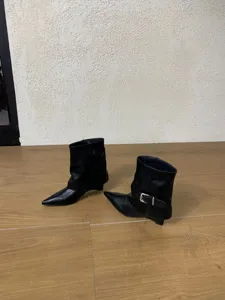 Schwarze Keilabsatz Stiefeletten Detailansicht mit Metallschnalle und glattem Leder.