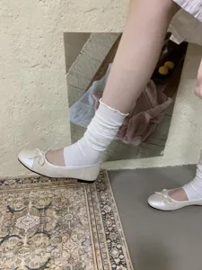 Primo piano di ballerine piatte da donna con fiocco abbinate a calzini bianchi su sfondo.