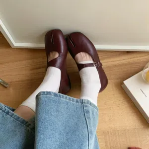 Detailed shot of brown split toe flat Mary Jane shoes paired with white socks and denim.