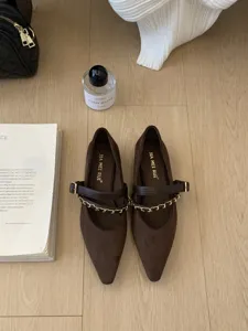Detailansicht dunkelbrauner spitzer Mary Jane Ballerinas mit Kettendetail auf Holz.